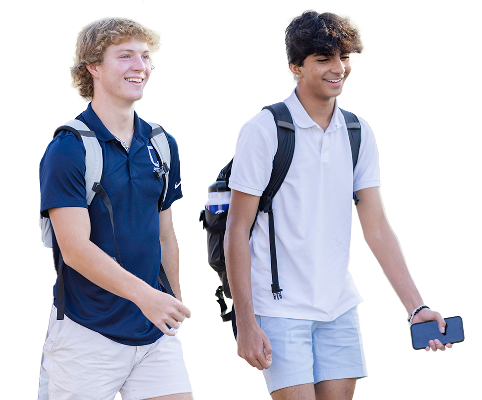 Two teenage boys walking outdoors, smiling, wearing backpacks, and casual summer clothing. One is holding a smartphone.