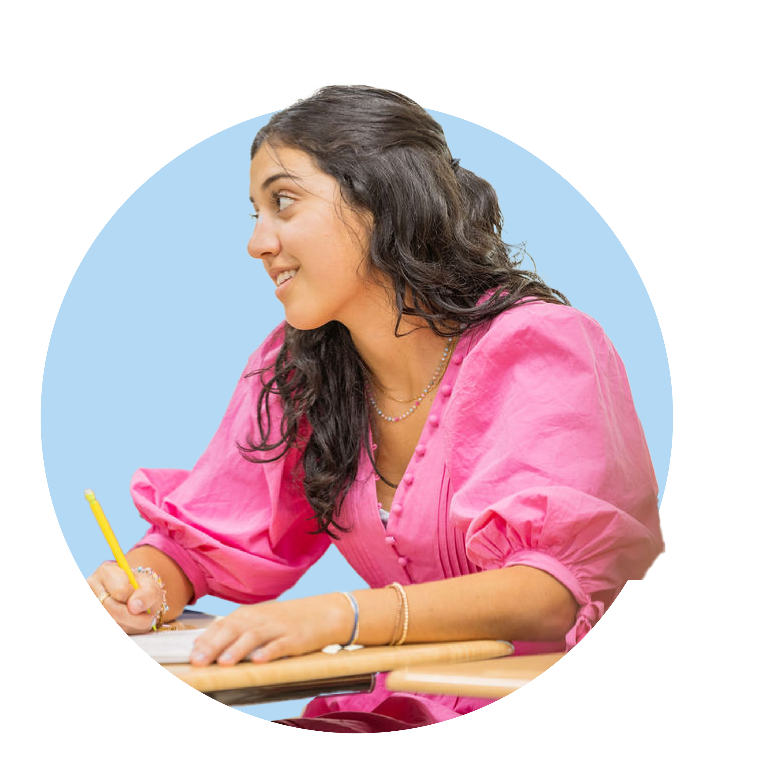 Young woman with dark curly hair wearing a pink blouse, smiling and writing with a yellow pencil at a wooden desk against a light blue circular background.