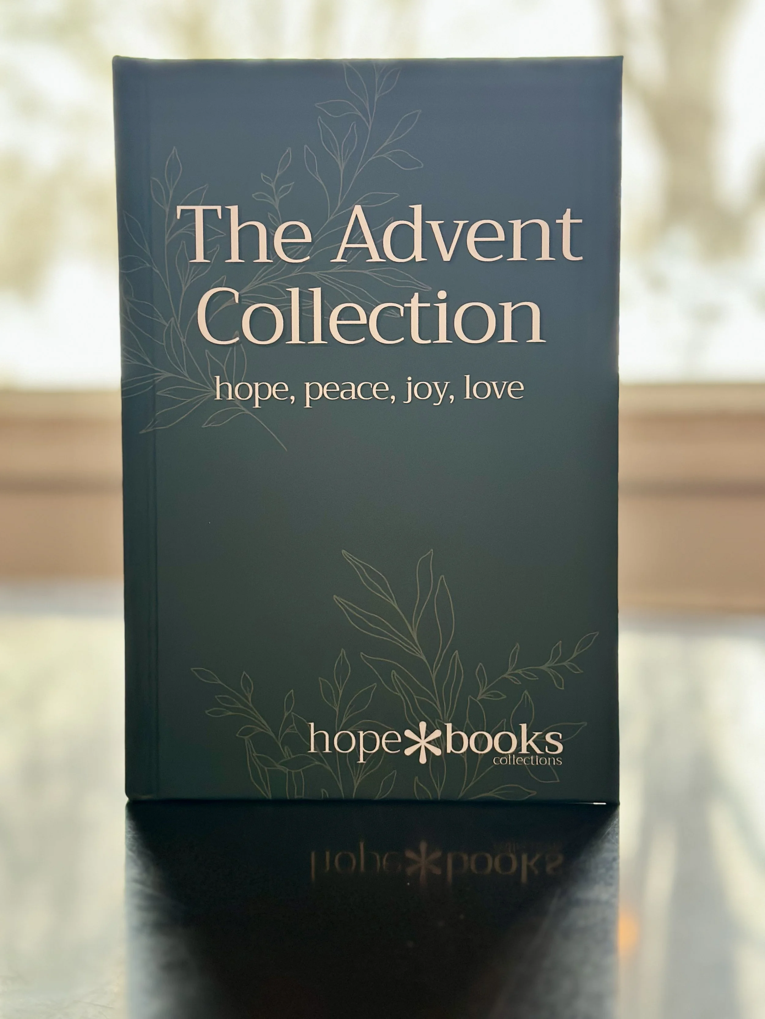 A minimalistic wall with a green eucalyptus branch on the left, a stack of books on the right, and a small jar on the bottom left, with the text 'New Collaboration Coming Soon' in the center.