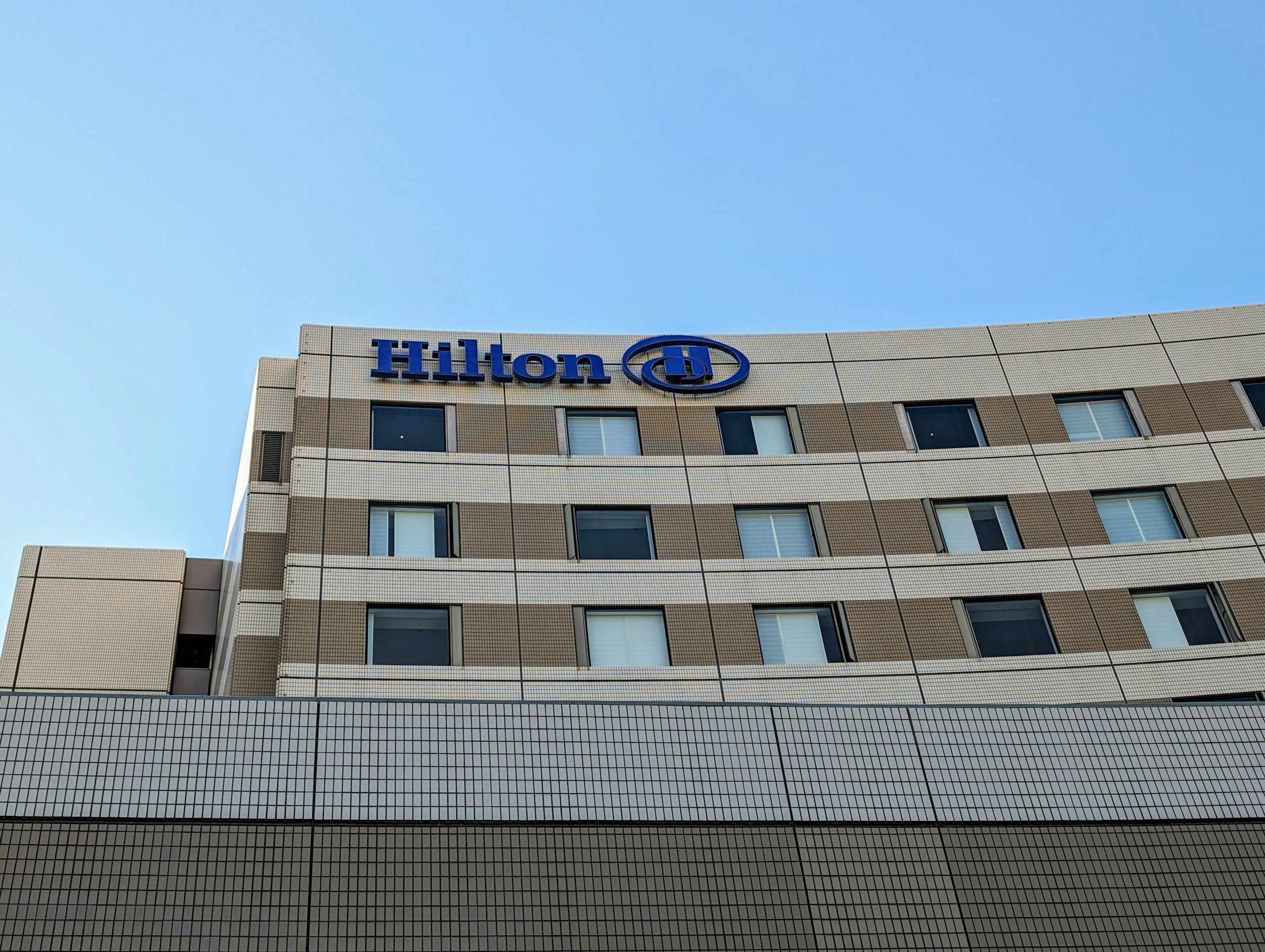 Hotel Hilton building with beige tiled facade and blue Hilton sign on top, under a clear blue sky