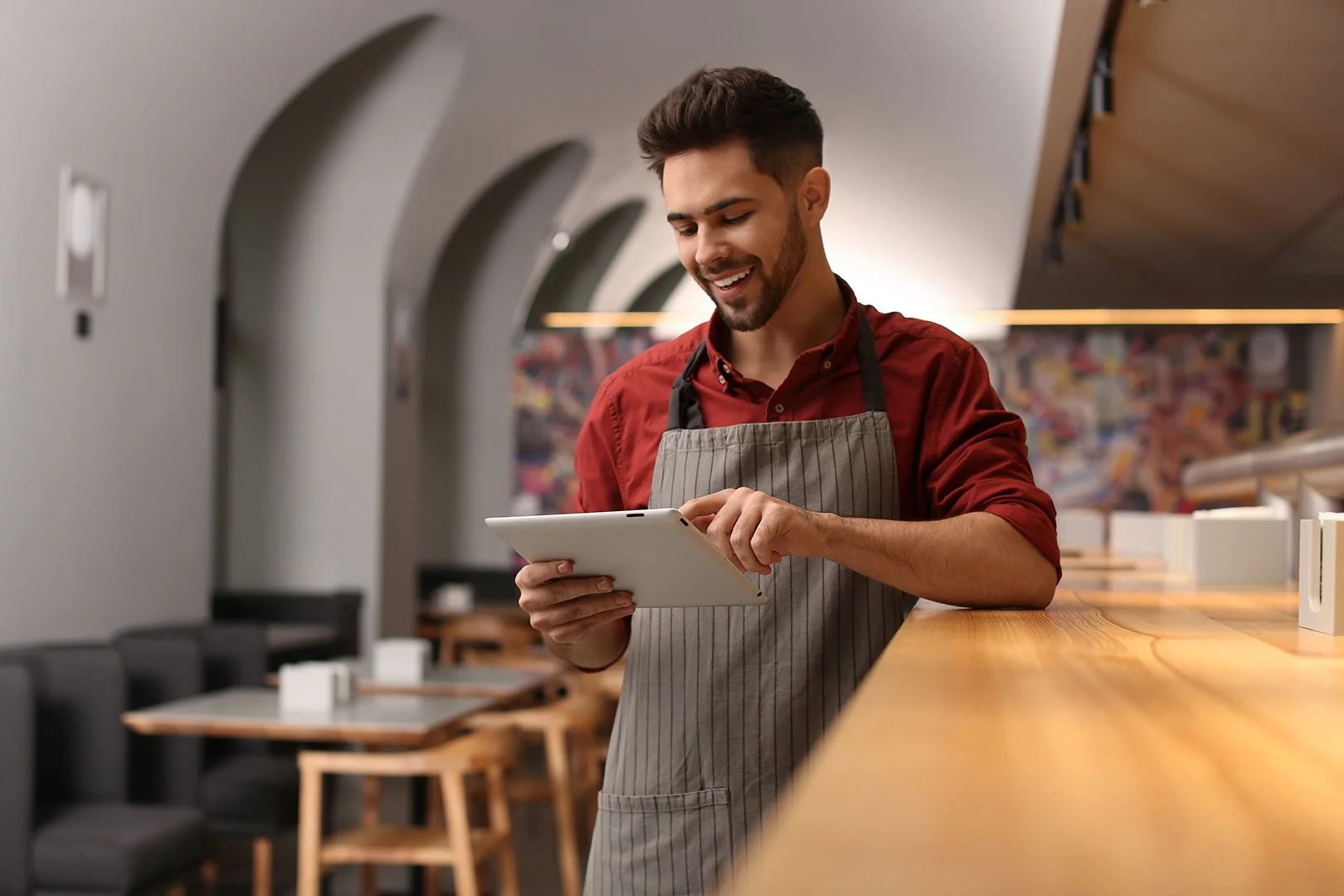 homme_tenant_un_ipad_avec_un_tablier_adosse_sur_un_bar_de_restaurant