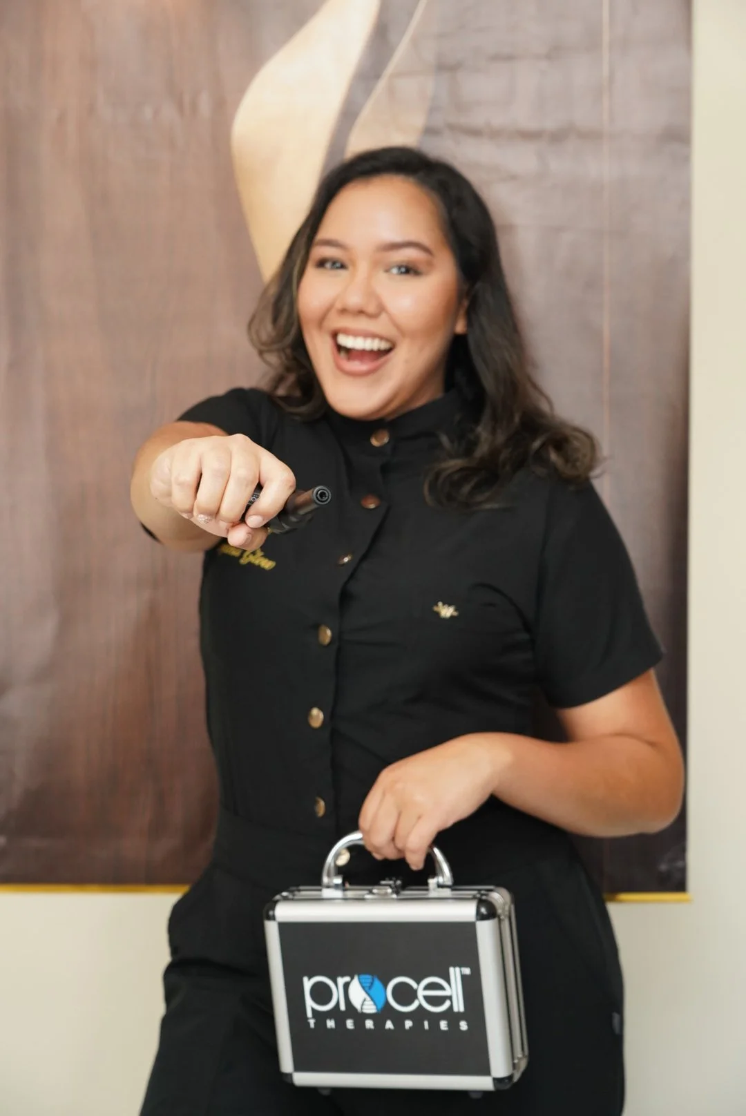 A woman smiling and pointing at the camera, holding a briefcase with the ProCell Therapies logo.