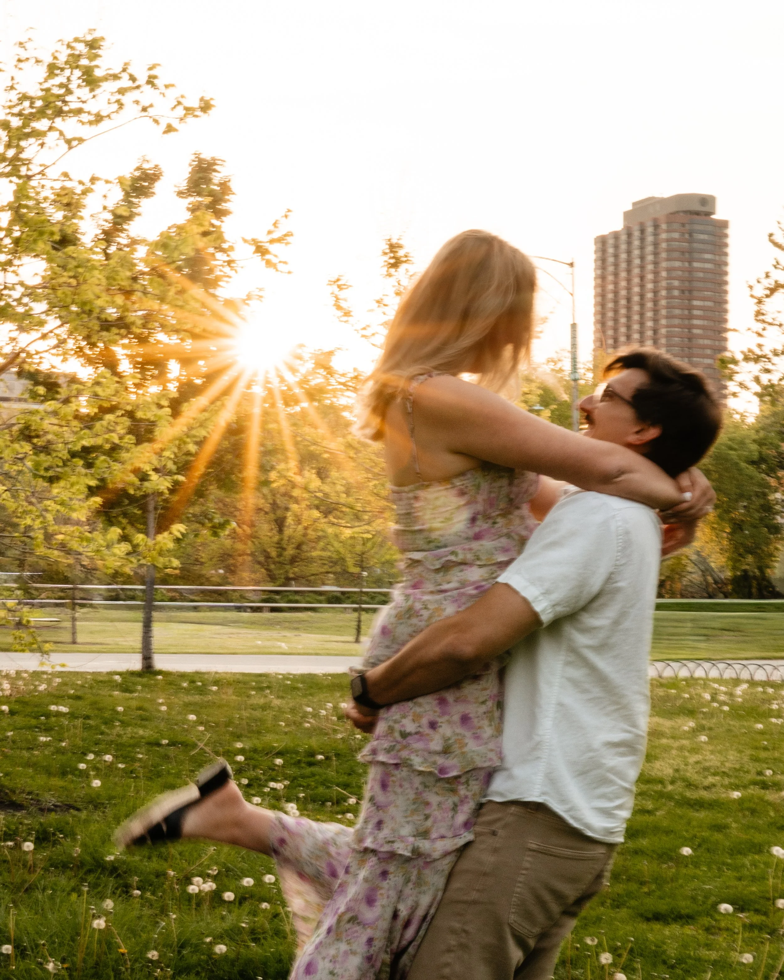 A man and woman dancing outdoors on a waterfront pier with a city skyline in the background.