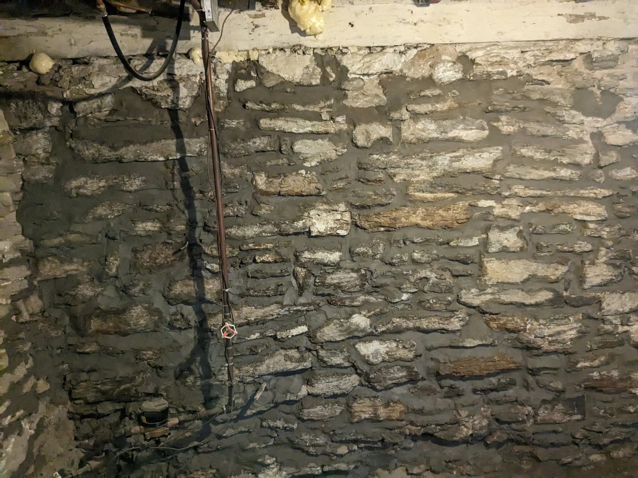 A stone wall with electrical wires and conduit running vertically, some insulation foam visible at the top.