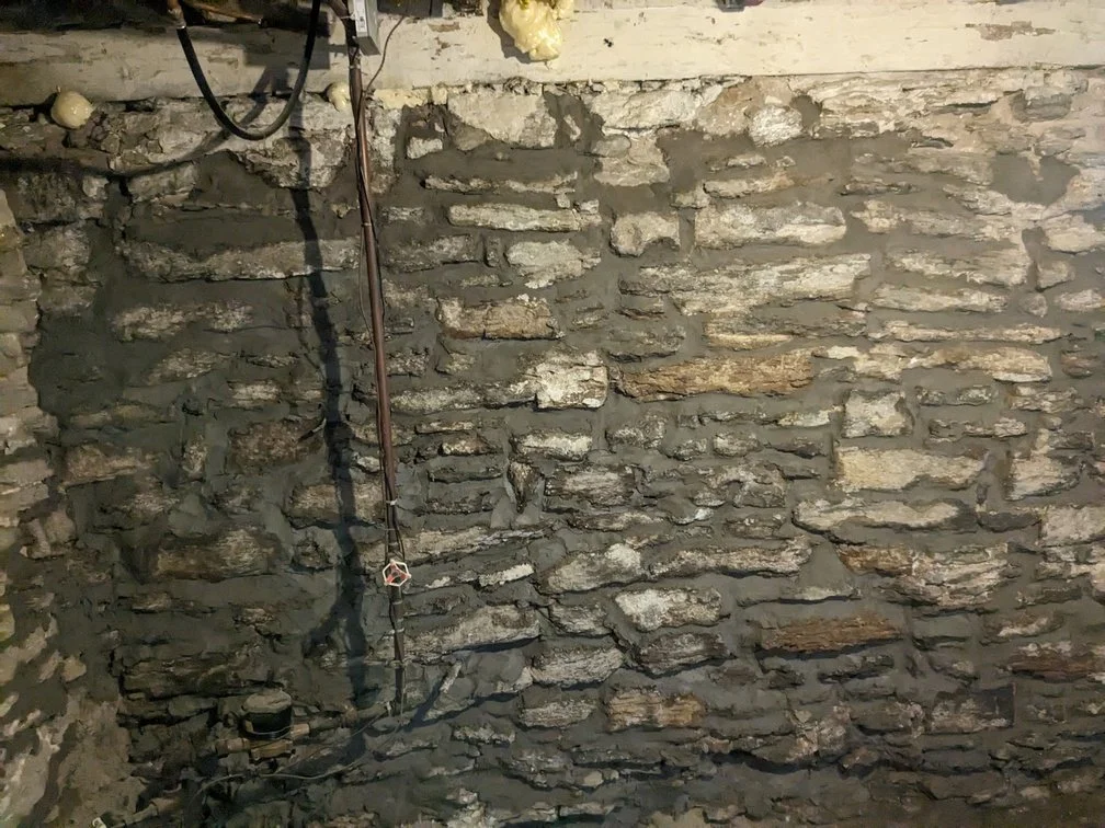 A rough stone wall with exposed wiring and pipes.