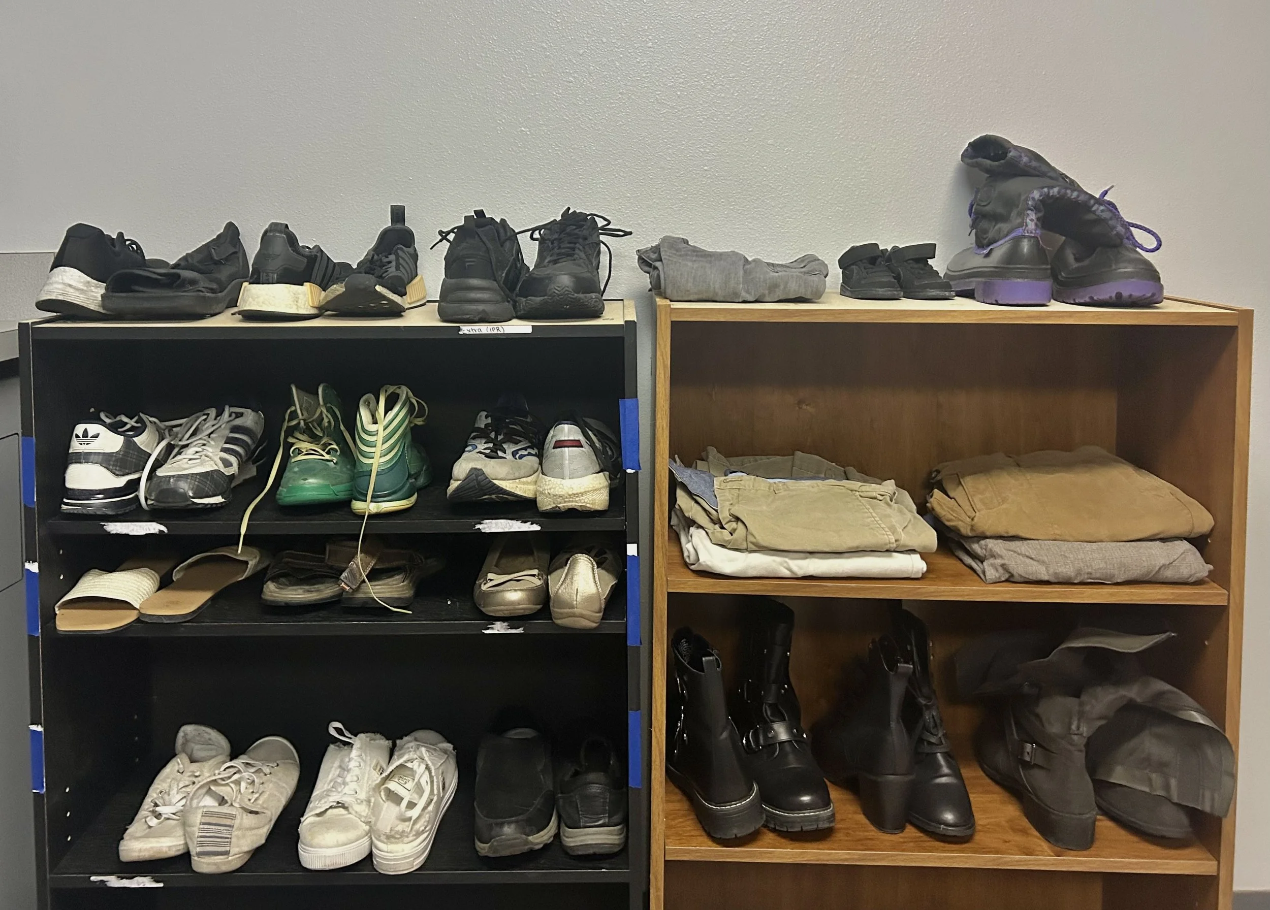 Two wooden shelves filled with various shoes and folded clothes against a white wall.