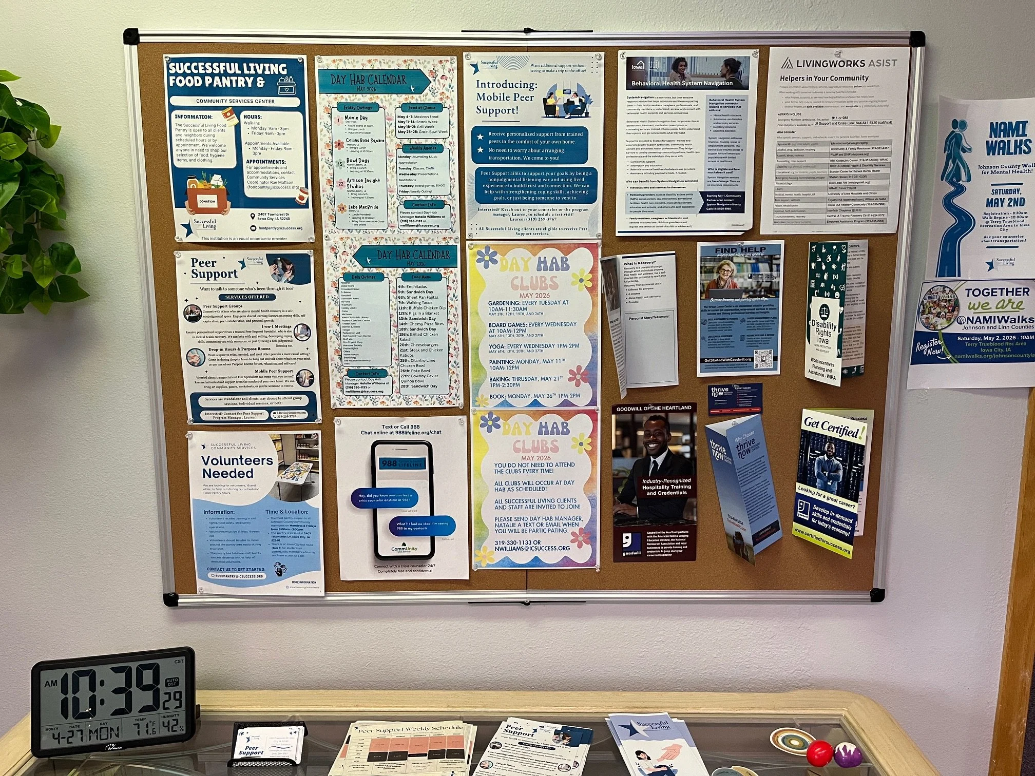 A bulletin board with various posters and flyers, including information about community services, support groups, schedules, and events. A digital clock displays the date and time as April 27, 2023, 10:39 AM.