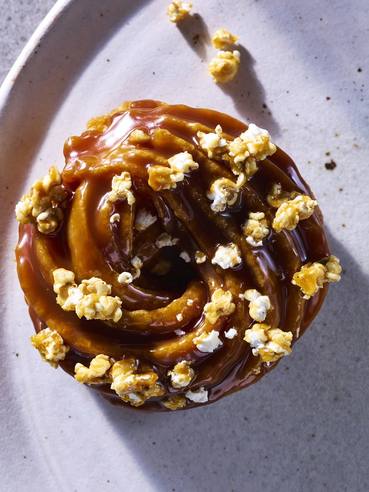 Top view of a cinnamon roll topped with caramel frosting and sprinkled with popcorn, on a white plate.