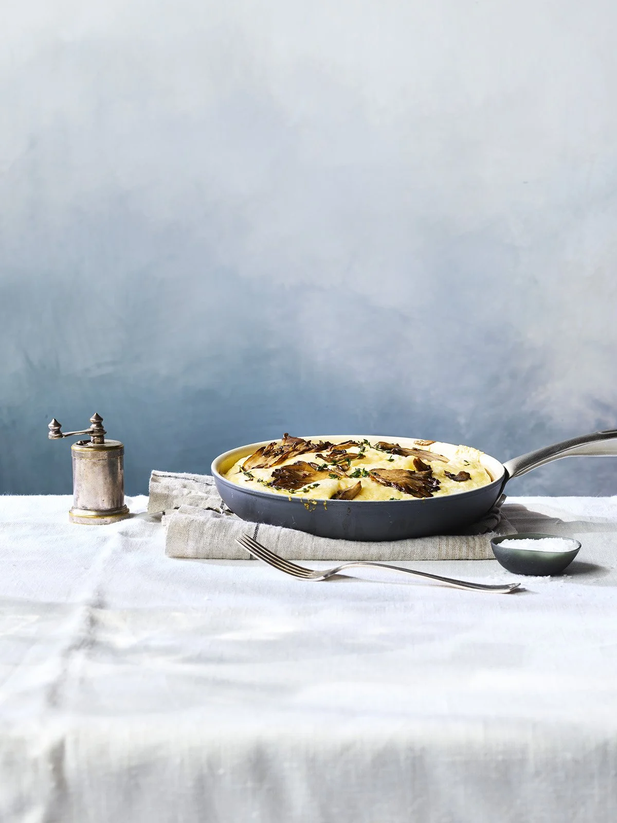 Fried chicken with mashed potatoes and gravy on a white tablecloth with a fork, salt shaker, and a small bowl of salt