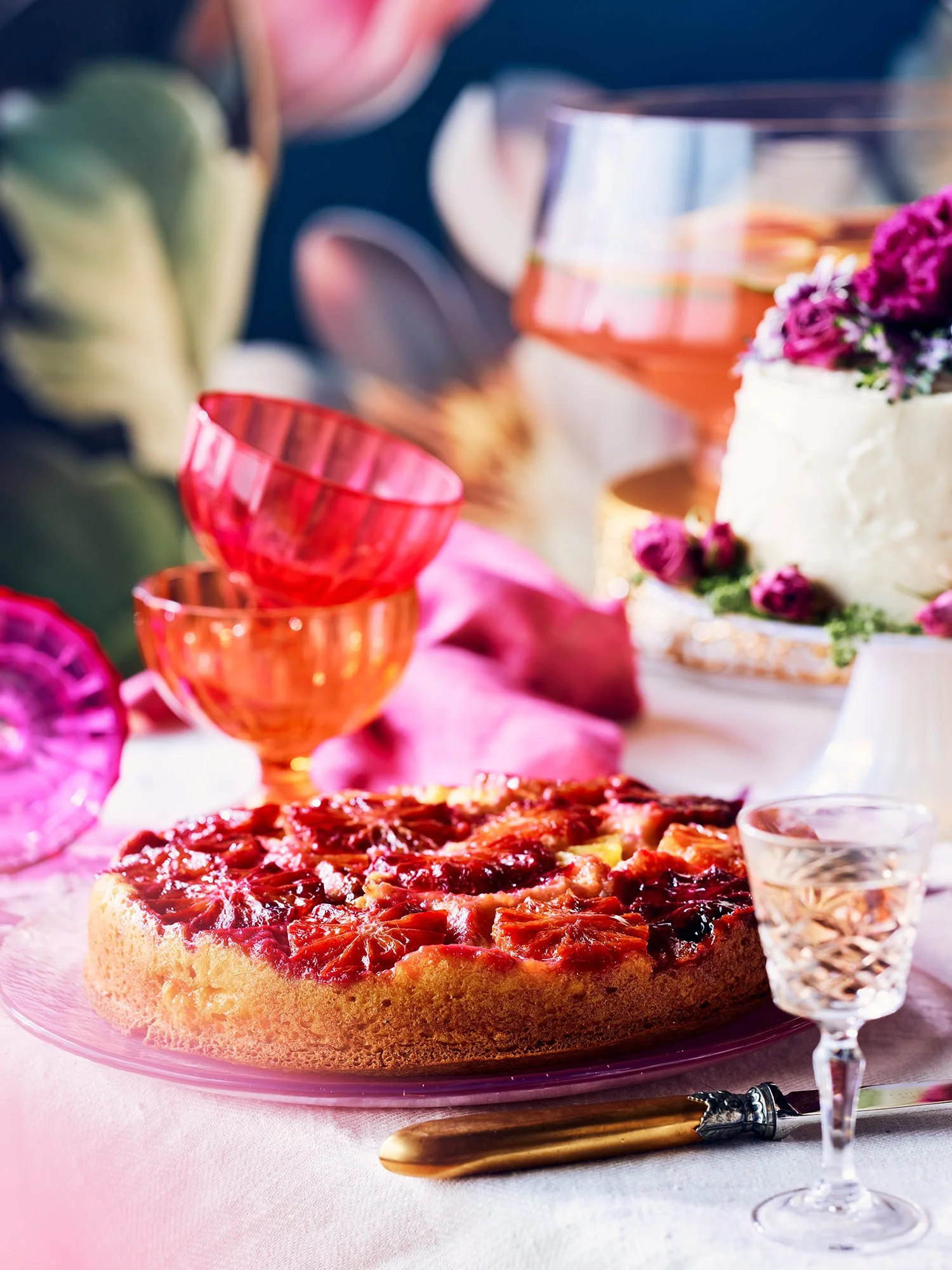 A table setting with a fruit tart, wine glasses, and floral decorations, suggesting a celebration or special occasion.