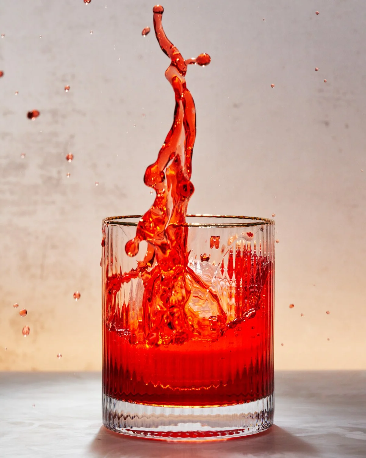 Red liquid splashing in a clear glass tumbler on a light surface with a neutral background.