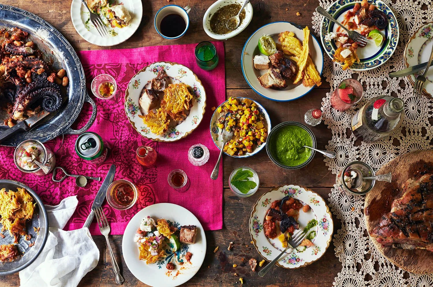 A table set with various dishes, including roasted octopus, casseroles, salads, and drinks, on colorful tablecloths and decor, indicating a festive meal.