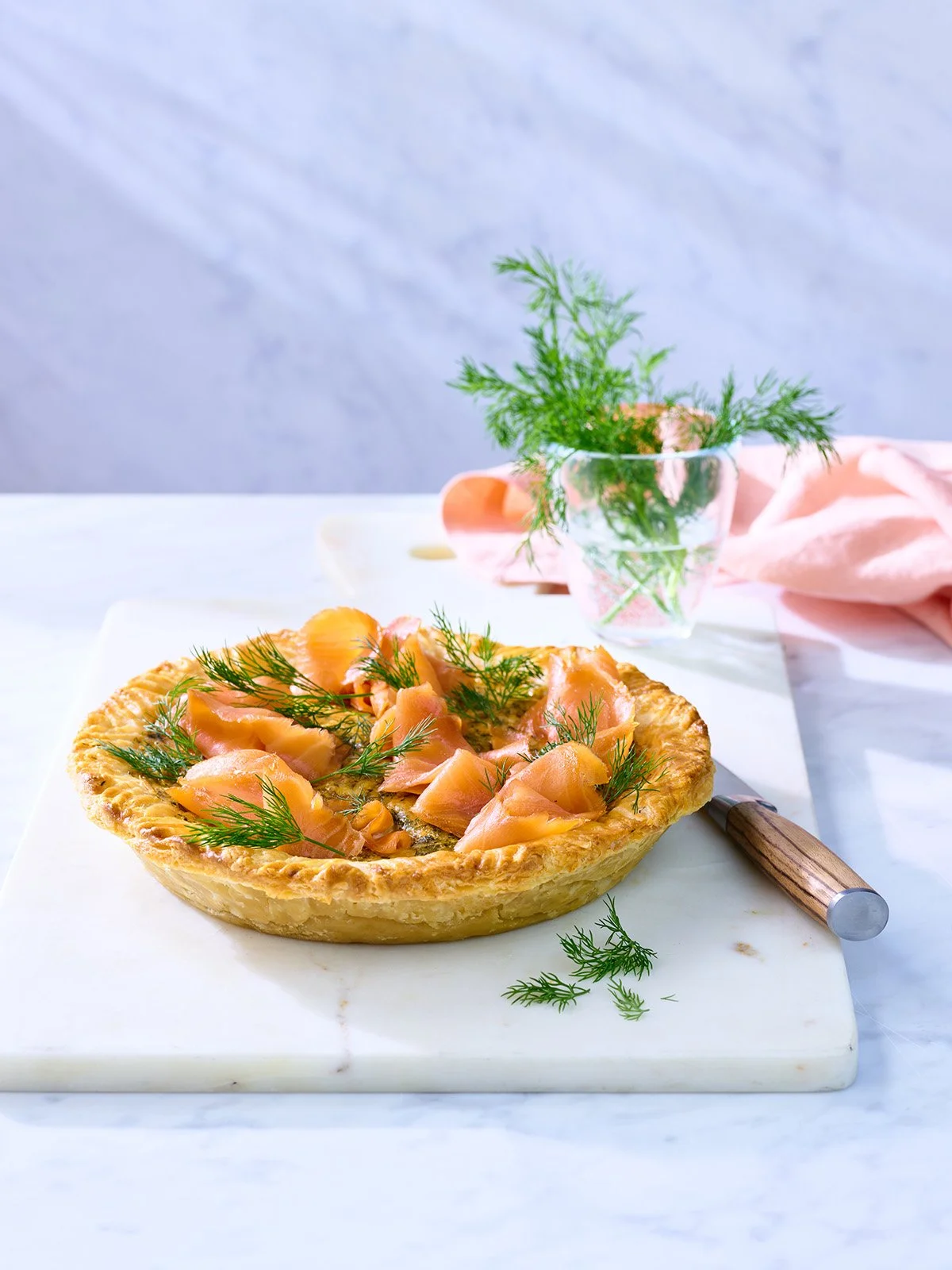 Salmon tart with dill on a marble cutting board, with a glass of water with dill in the background.