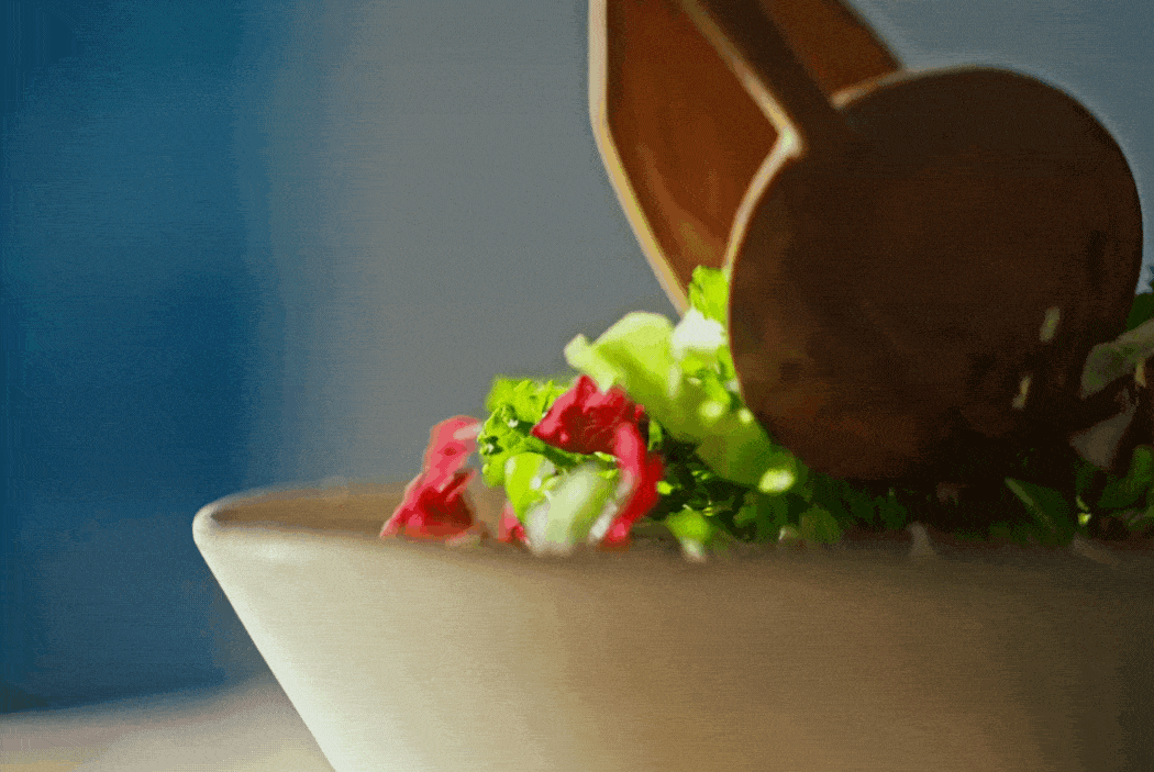 A white bowl with shredded lettuce, diced tomatoes, and sliced cucumbers, with a brown sauce container tipped over pouring sauce onto the salad.