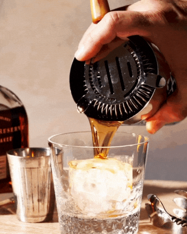 Pouring a drink into a glass with ice, using a cocktail shaker.