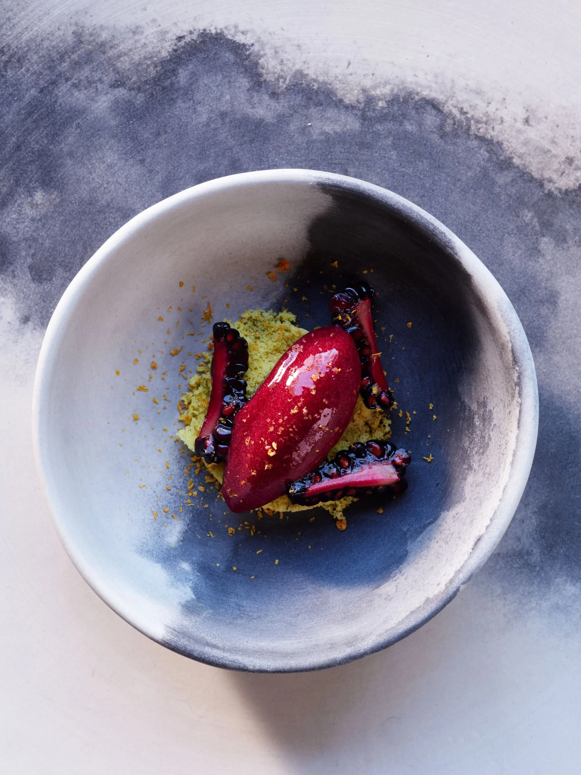 Dessert served in a bowl with a red sorbet, blackberries, and yellow crumbles.