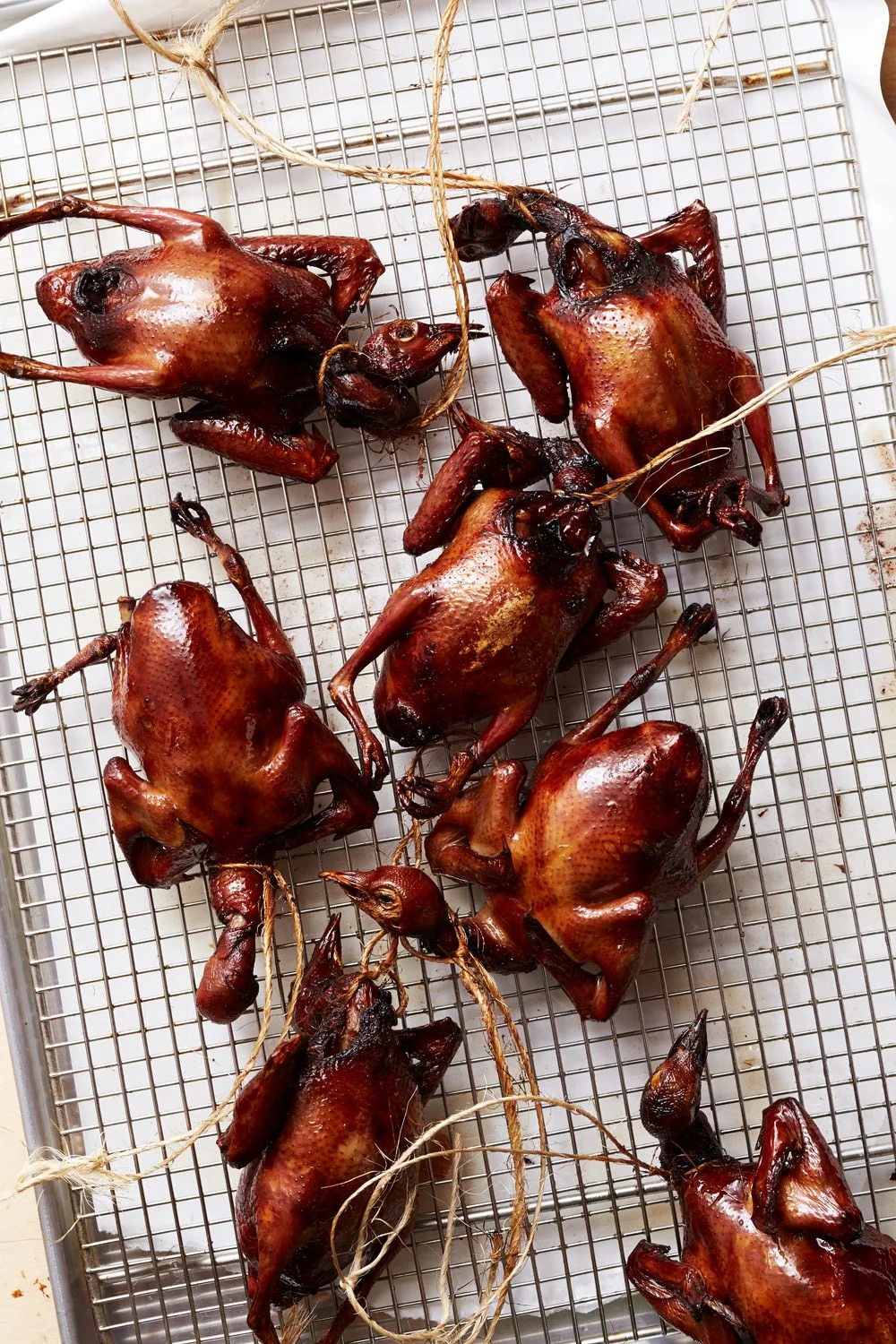 Five roasted quail birds with dark, shiny, crispy skin on a wire rack.