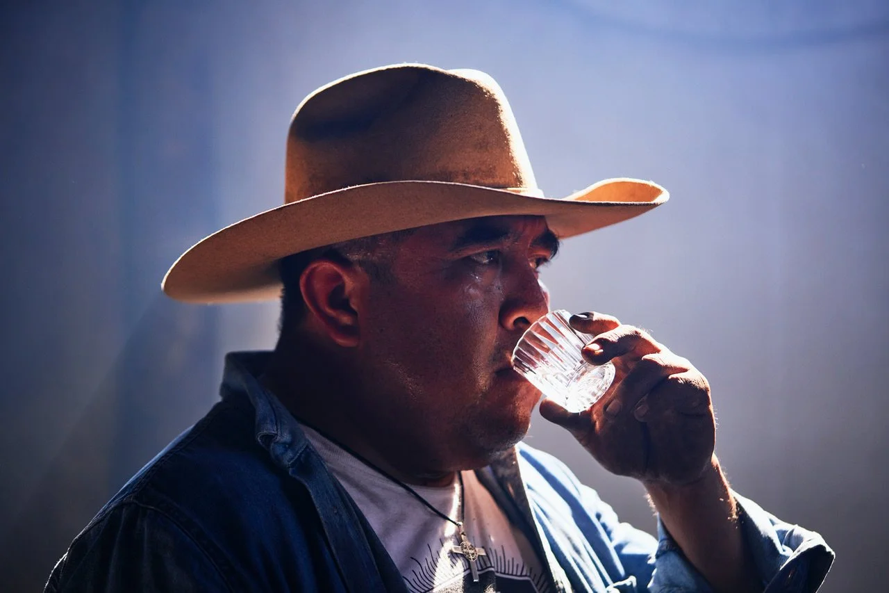 Man wearing a cowboy hat drinking from a glass of whiskey