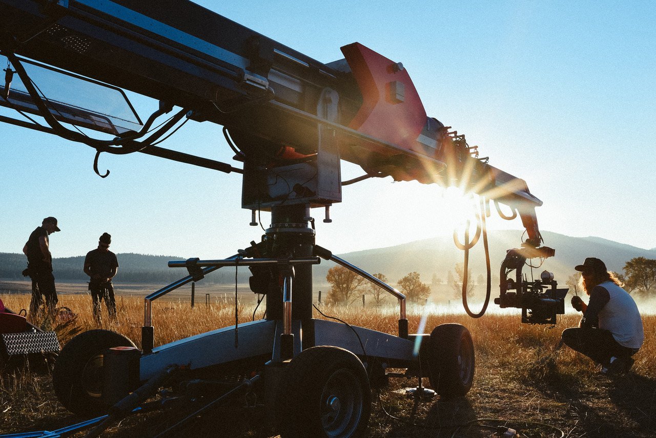 Filming crew operating camera equipment in an open field at sunset.