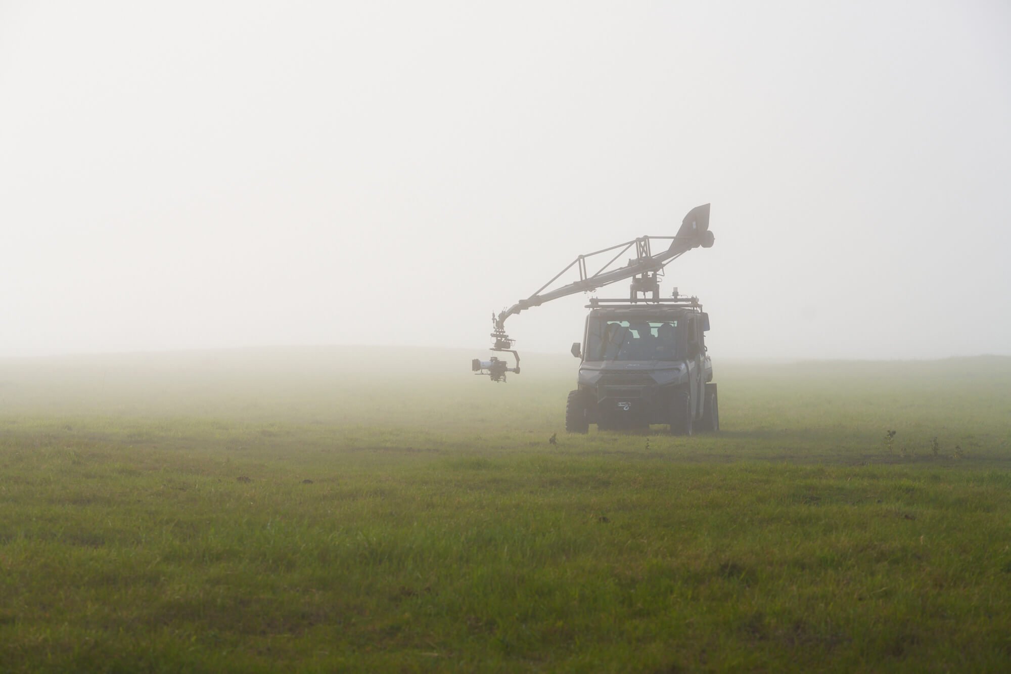 A camera mounted on a crane attached to a small off-road vehicle in a foggy grassy field.