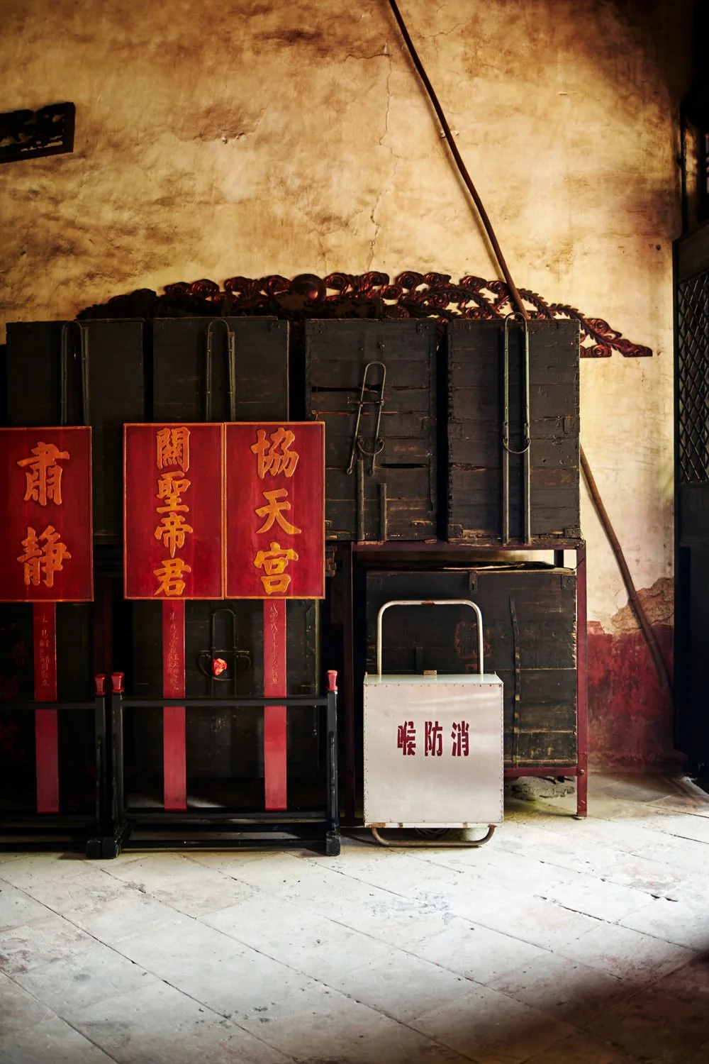 Old wooden crates, red banners with Chinese characters, and a metal box with more Chinese characters, all against a weathered wall.