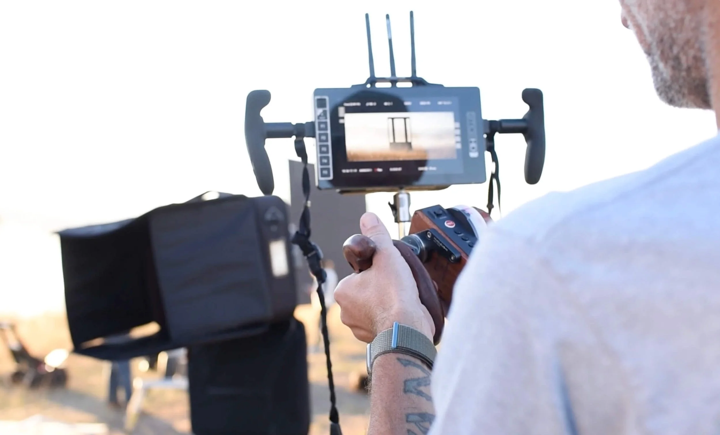 A person operating a camera gimbal stabilizer on a video camera outdoors during sunset.