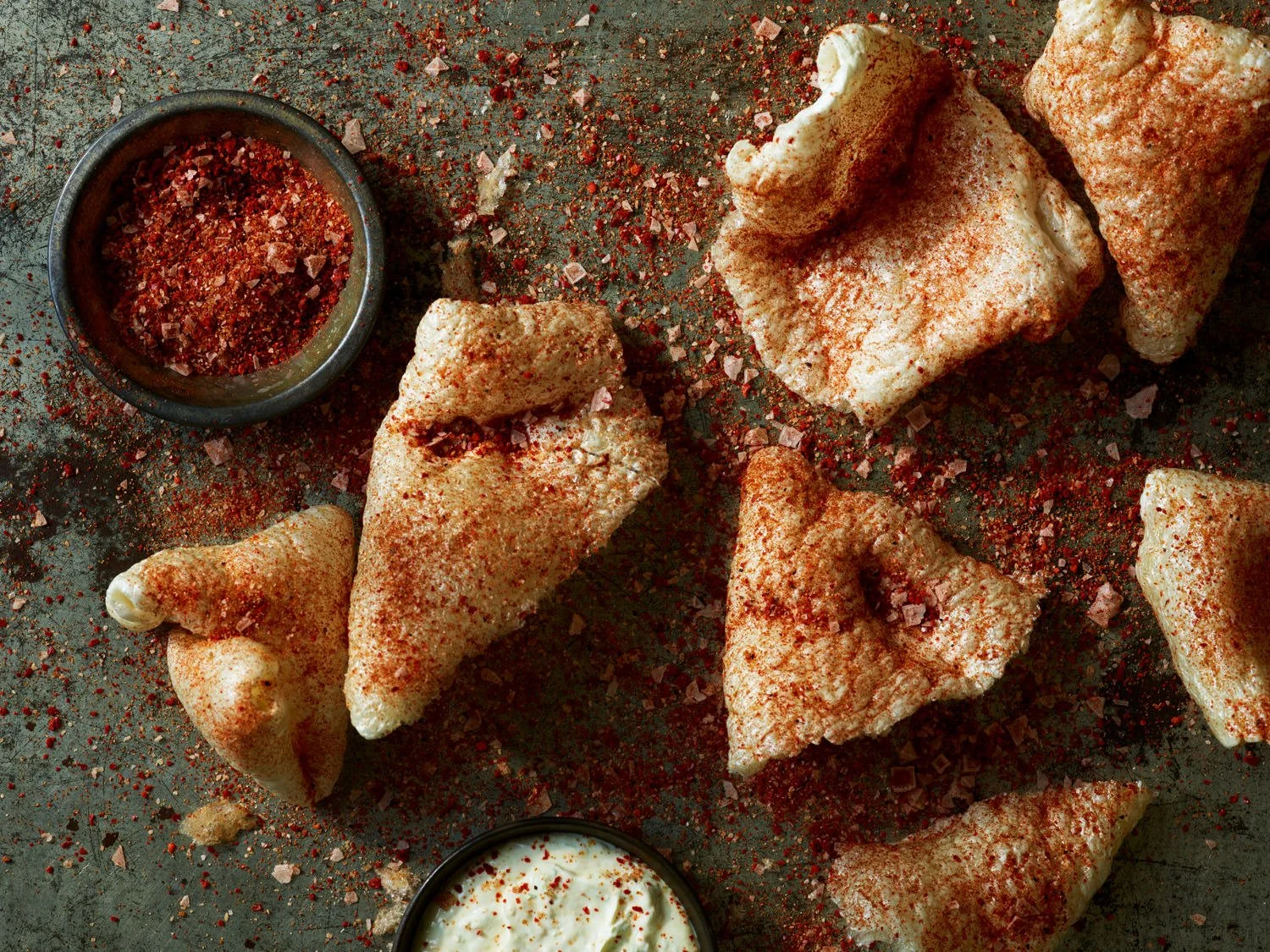Battered fried chicken pieces with red seasoning and crushed red pepper flakes, served with a bowl of creamy dipping sauce.