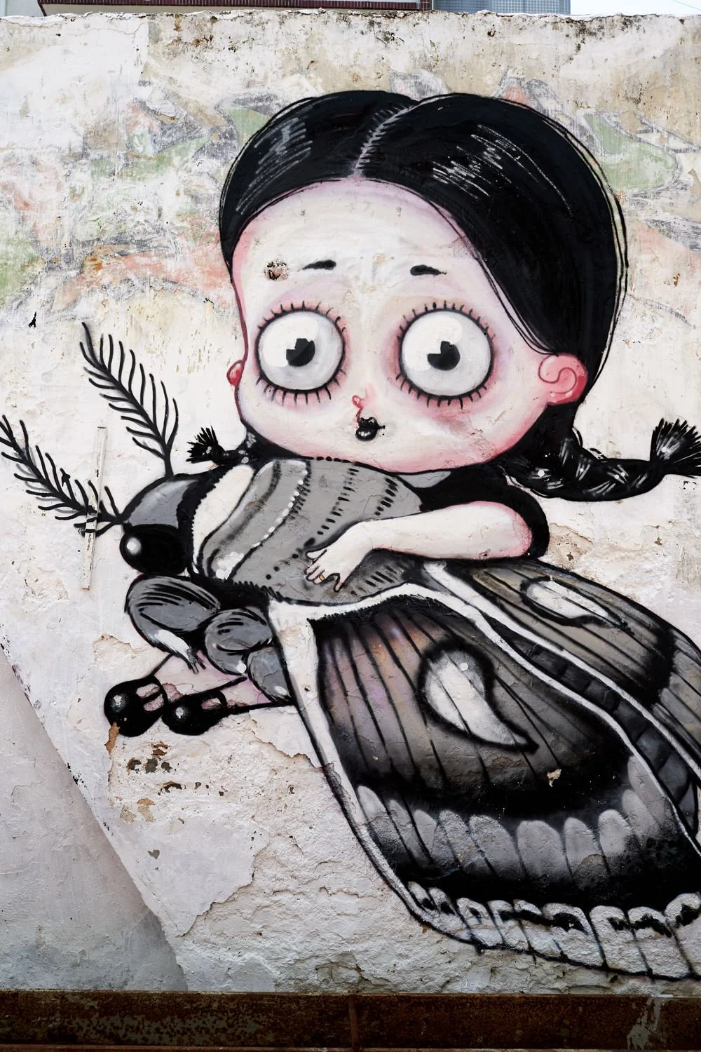 Street art of a cartoon girl with large eyes and black hair, holding a butterfly on a wall.