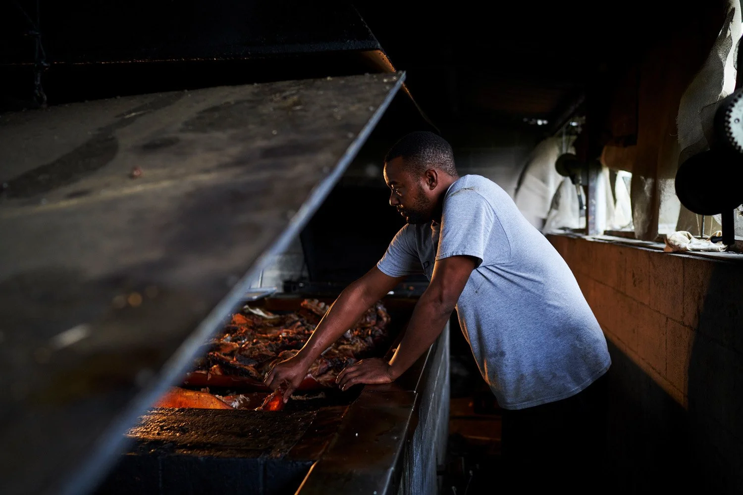 Man cooking over an open fire with meat on skewers in a rustic setting.