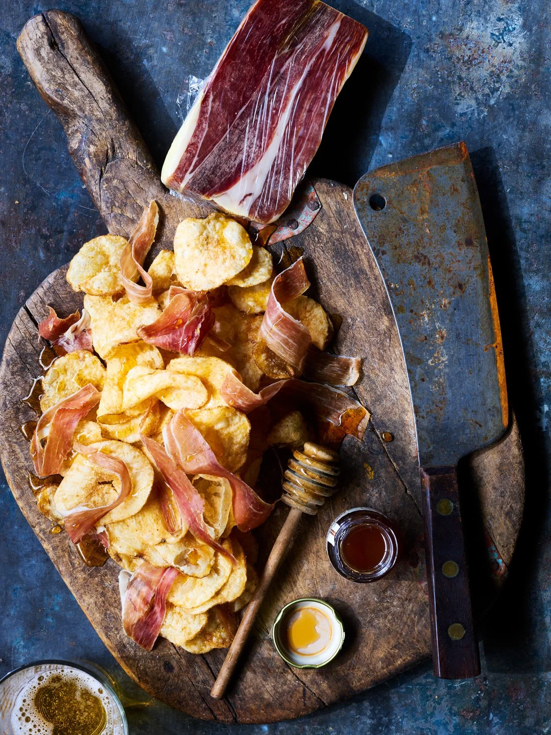 Pizza fries topped with prosciutto, honey dip, and beer on a rustic wooden serving board.