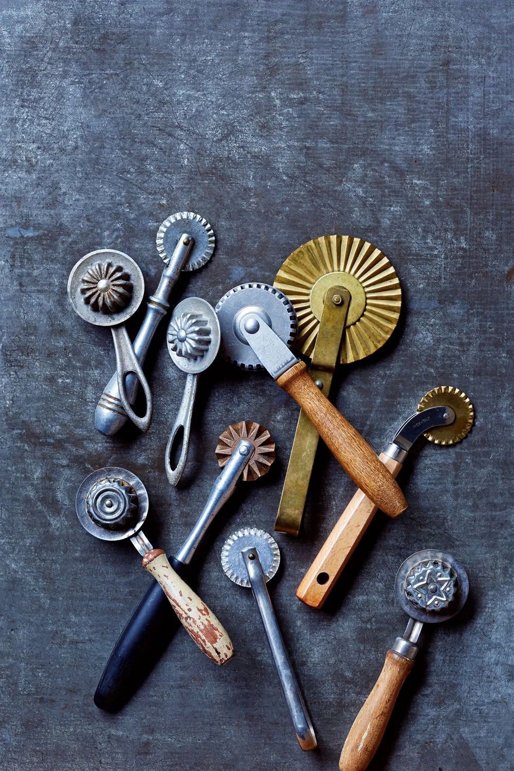 Assorted vintage pastry cutters with metal and wooden handles, arranged on a textured gray surface.