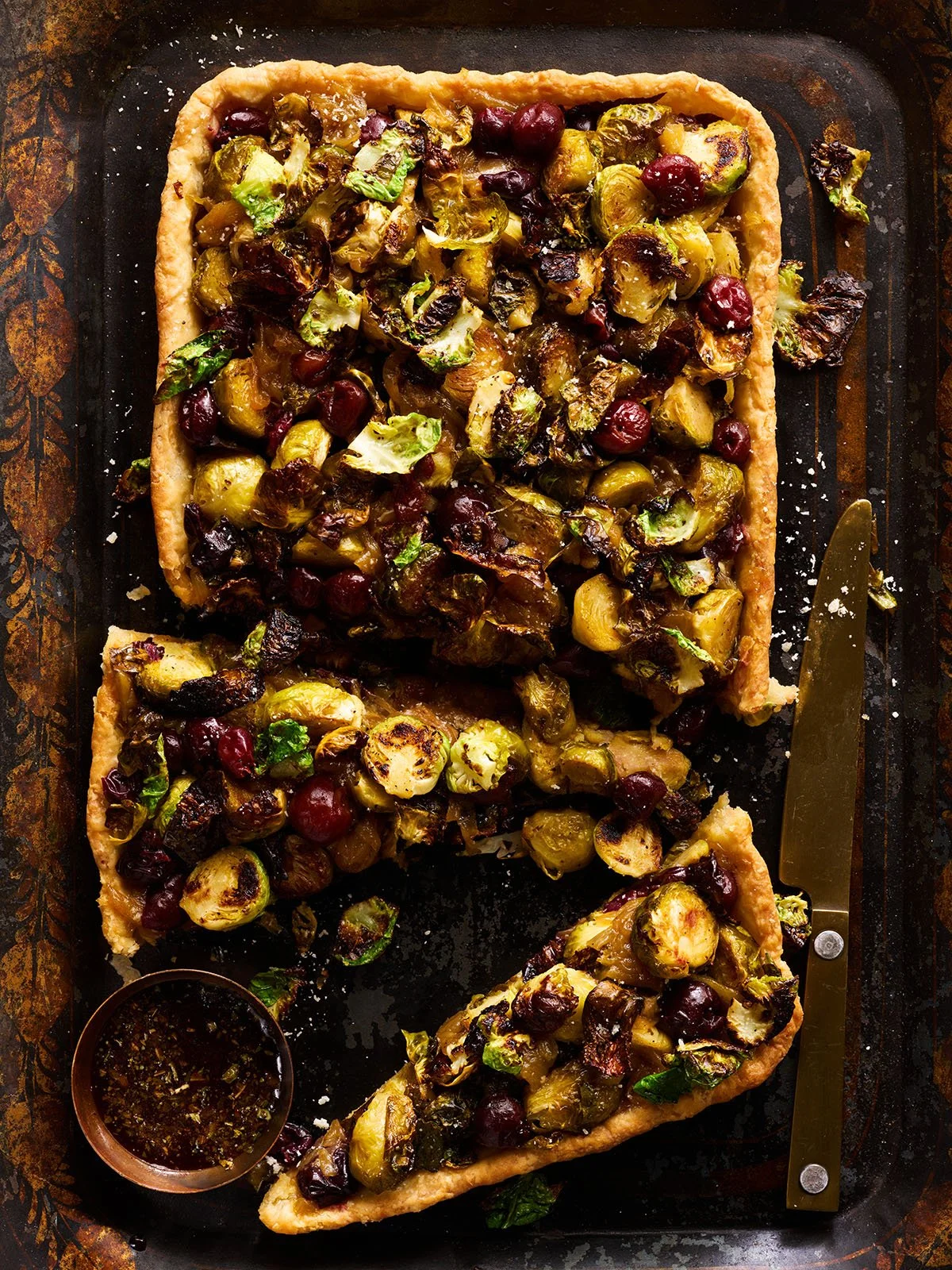 Baked Brussels sprout tart with chopped Brussels sprouts, cranberries, and herbs on a baking sheet, with a slice cut out.