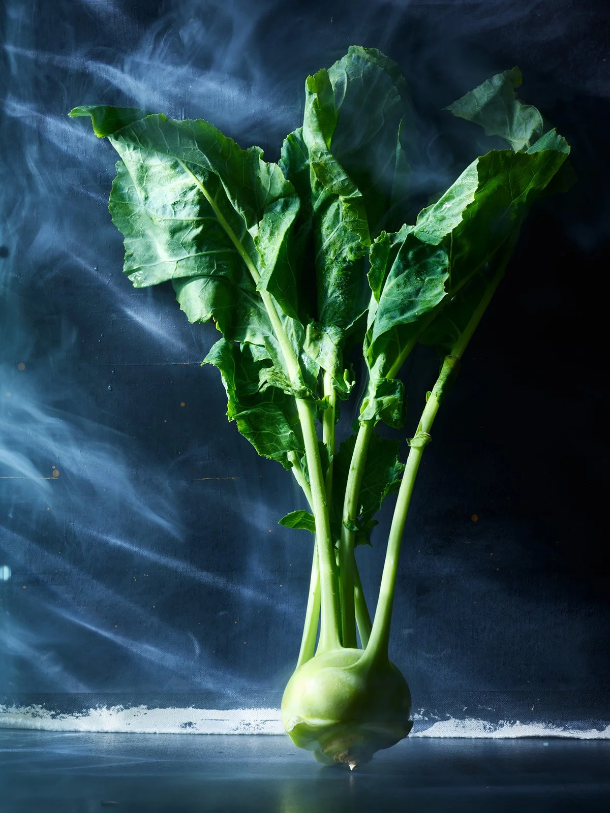 Fresh kohlrabi with green leaves against a dark background.