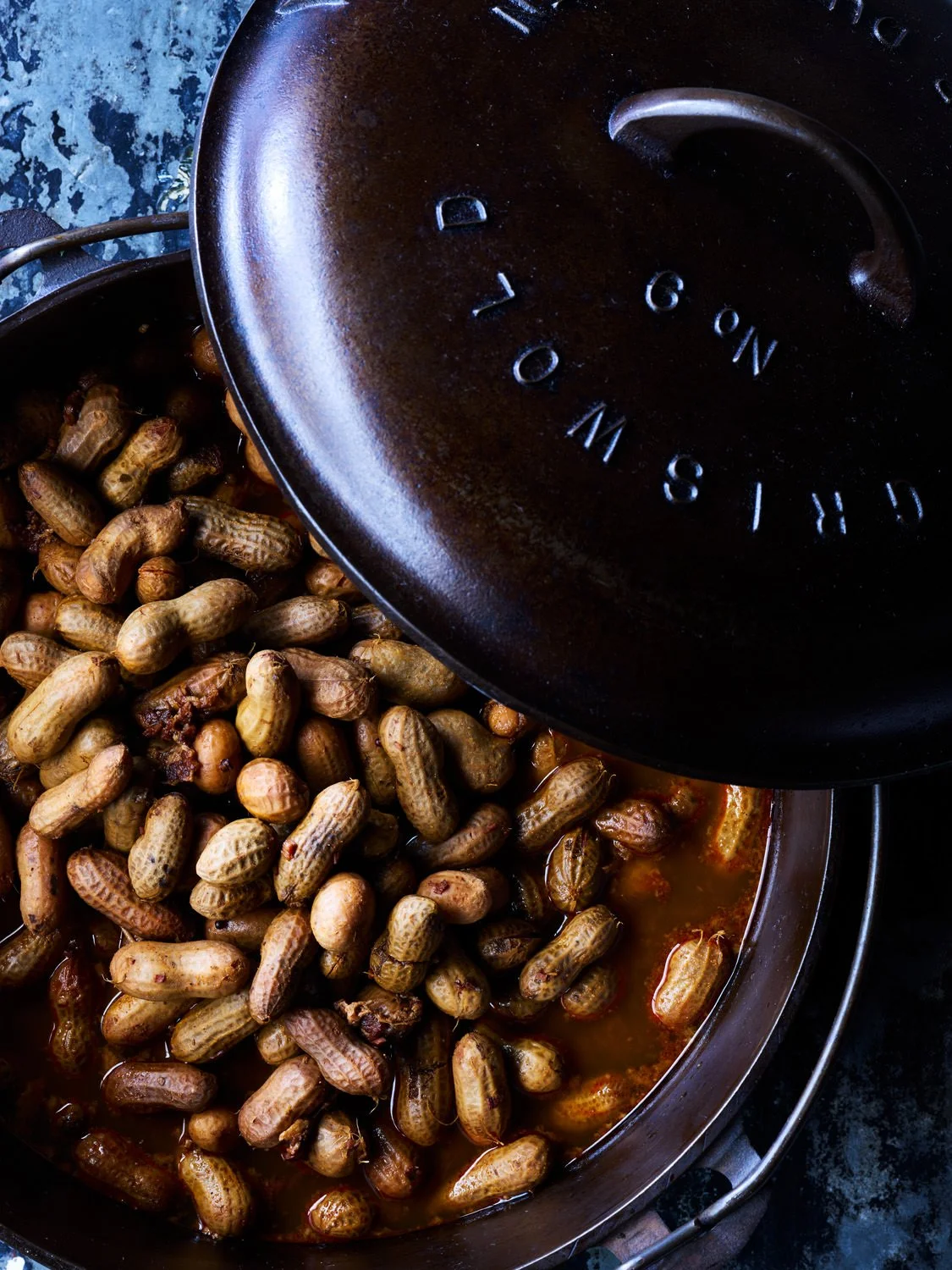 Cooking peanuts in a cast iron skillet with a lid. The lid is partially open showing the peanuts inside.