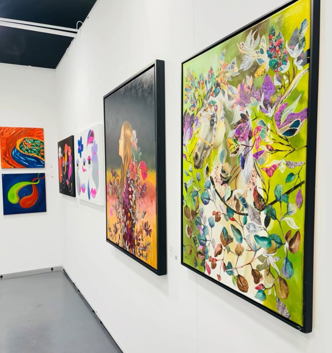 Une galerie d'art avec plusieurs peintures abstraites et figuratives colorées accrochées à un mur blanc.