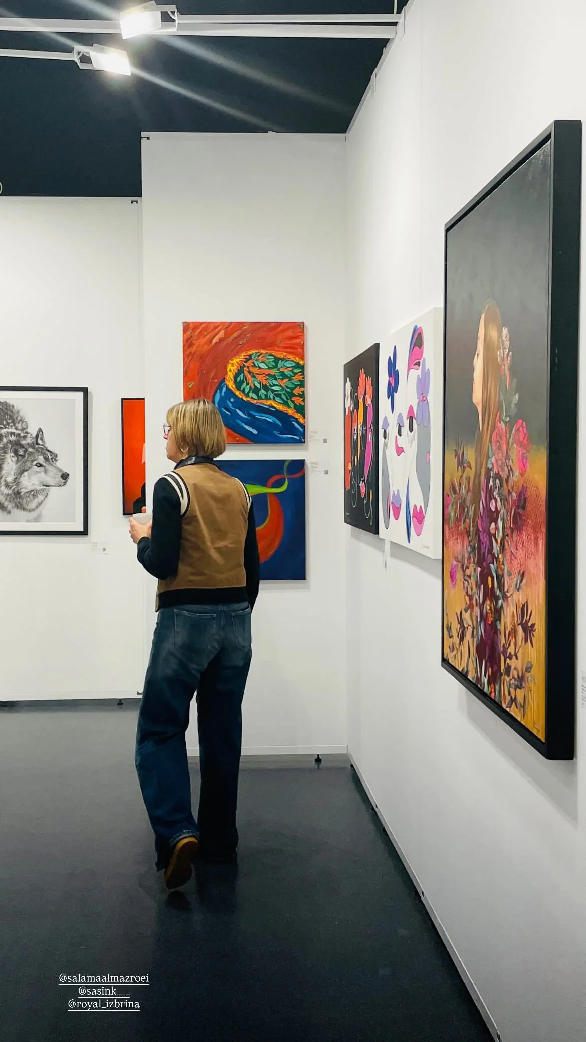 Une femme dans une galerie d'art contemporaine observant plusieurs tableaux colorés et figuratifs.