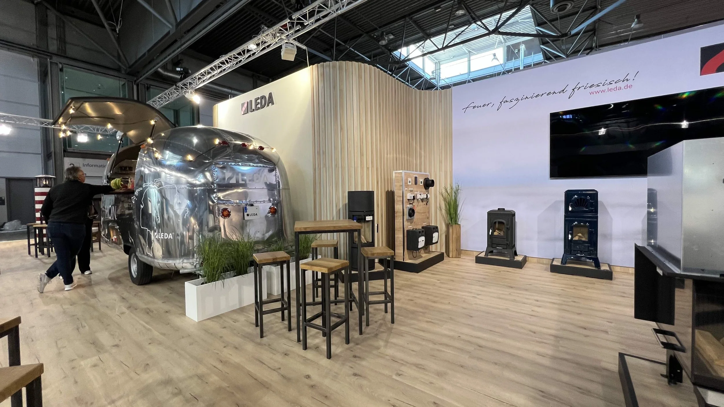 Ausstellungsstand von Leda mit einem silbernen retro Metall-Airstream-Truck, Pflanzen, Stehtischen, Heizgeräten und einem großen Bildschirm in einem Messegebäude