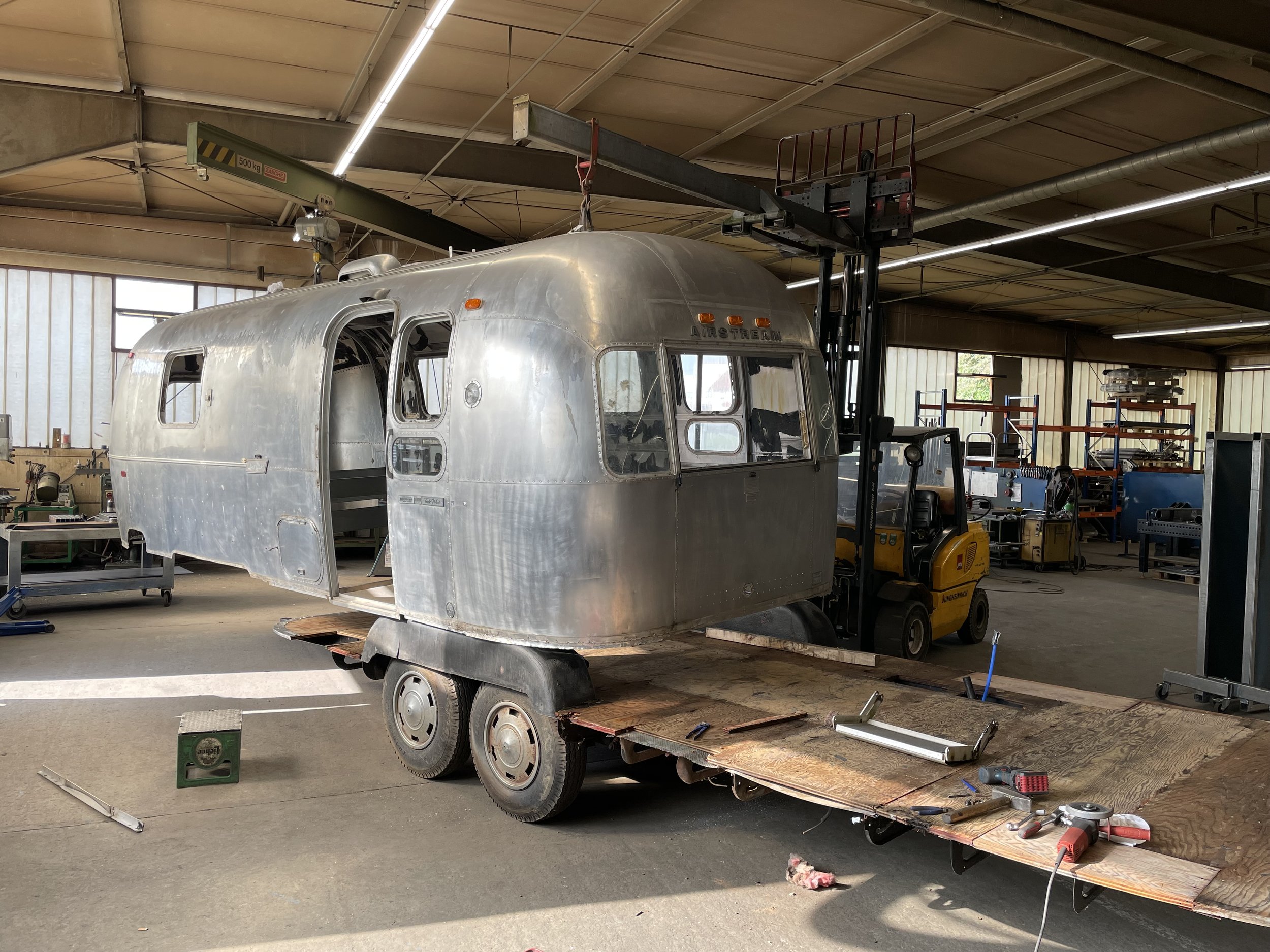 Ein historisches Aluminium-Reisehüttenfahrzeug in einer Werkstatt, das auf einem Wagen steht, während der Innenraum renoviert wird.