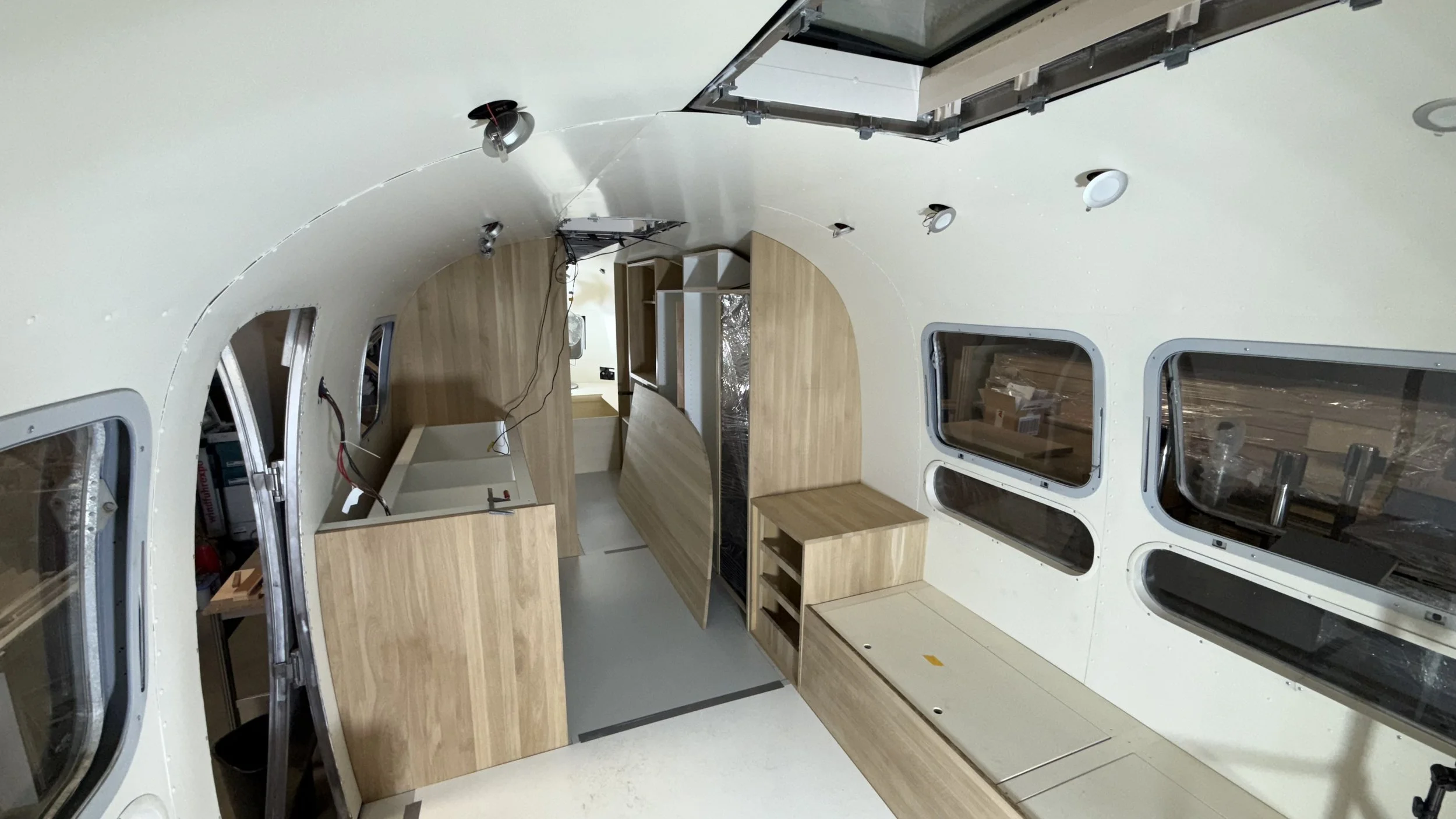 Innenansicht eines Gebäudes im Bau, mit Holzarbeiten, Fenstern und Installationsarbeiten.