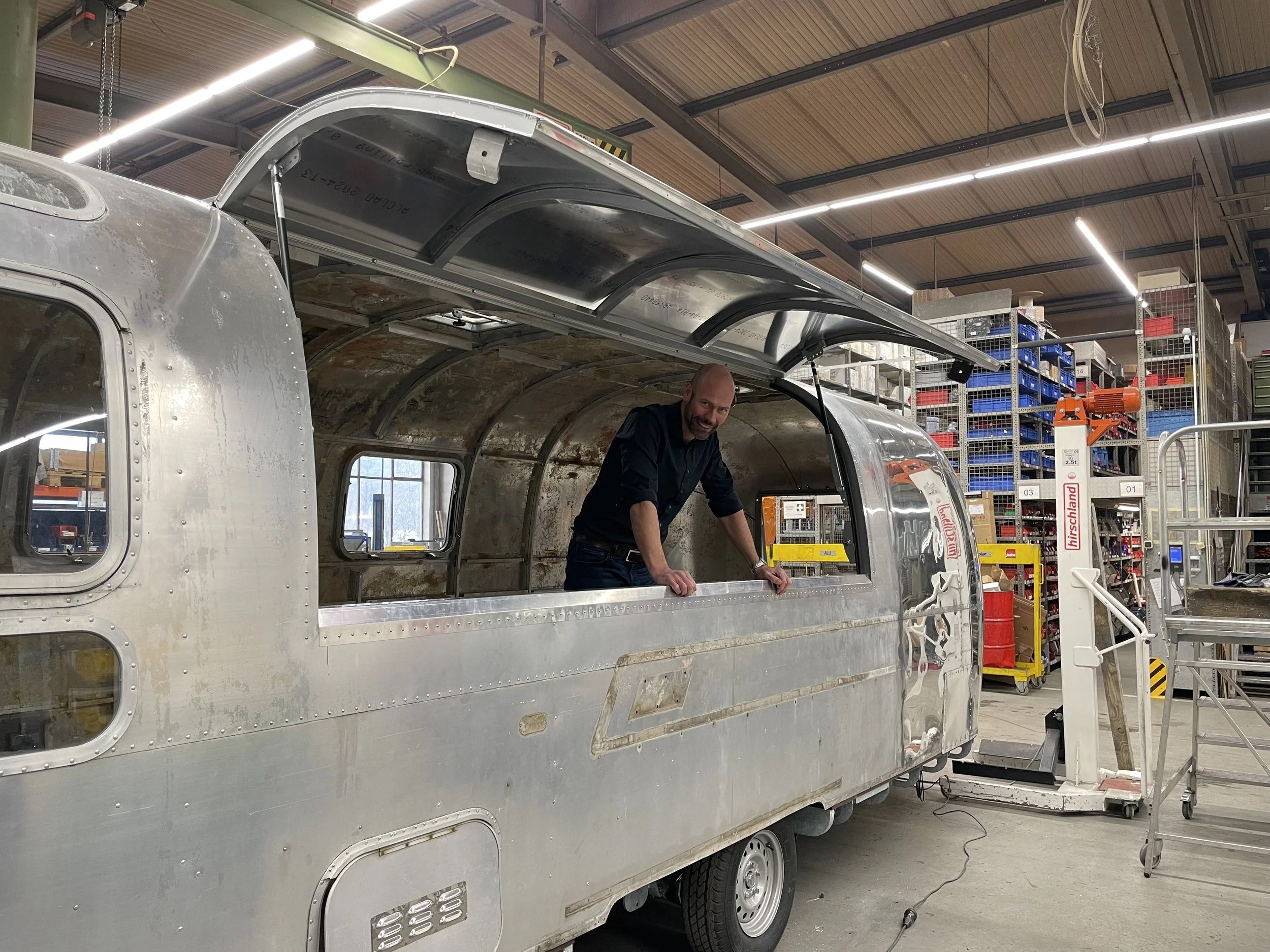 Ein Mann steht in einem metallischen Wohnwaggon, der in einer Werkstatt im Bau ist.