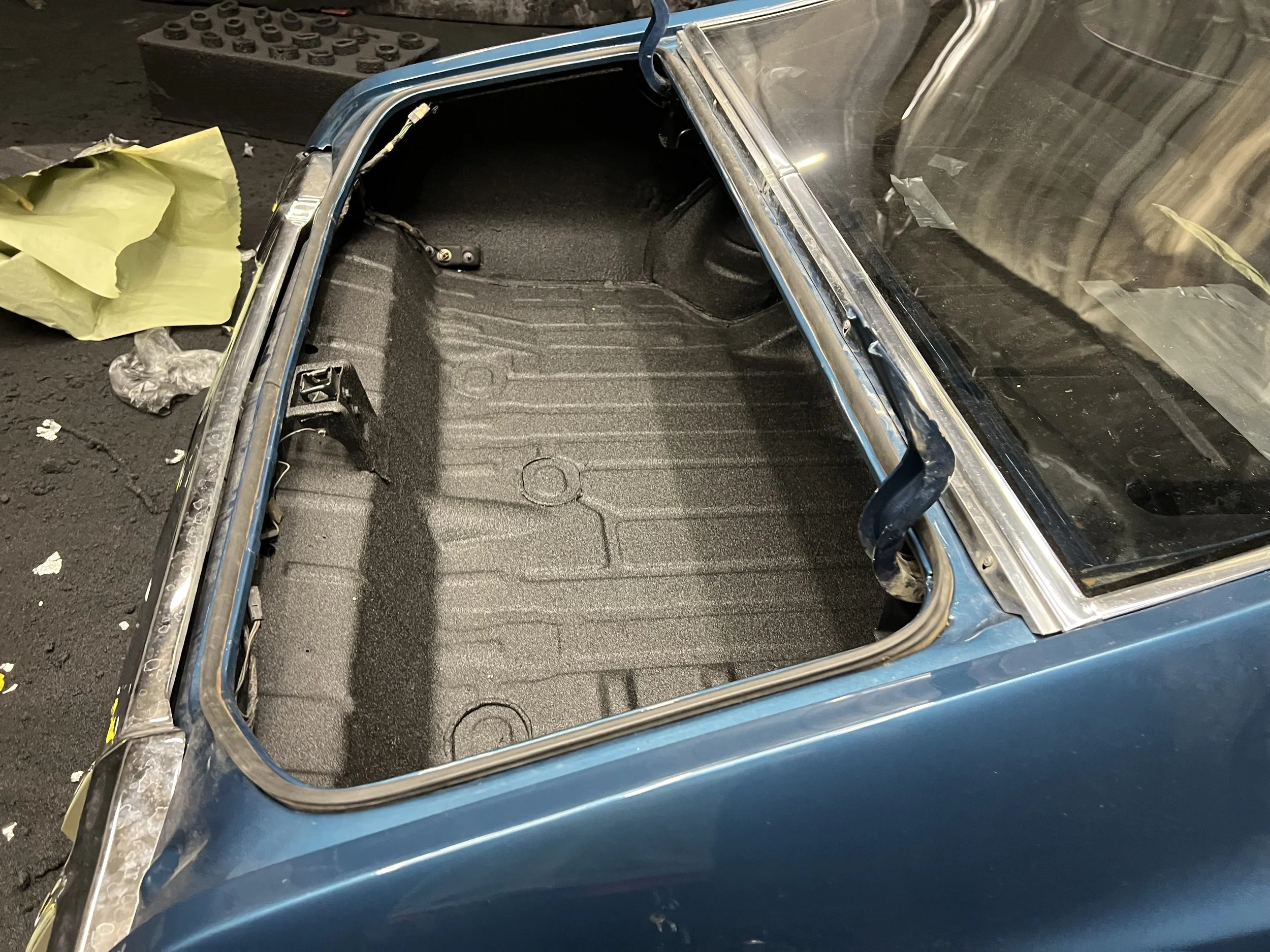 Empty car trunk with the roof open, showing a black textured interior surface and some tools and parts nearby.