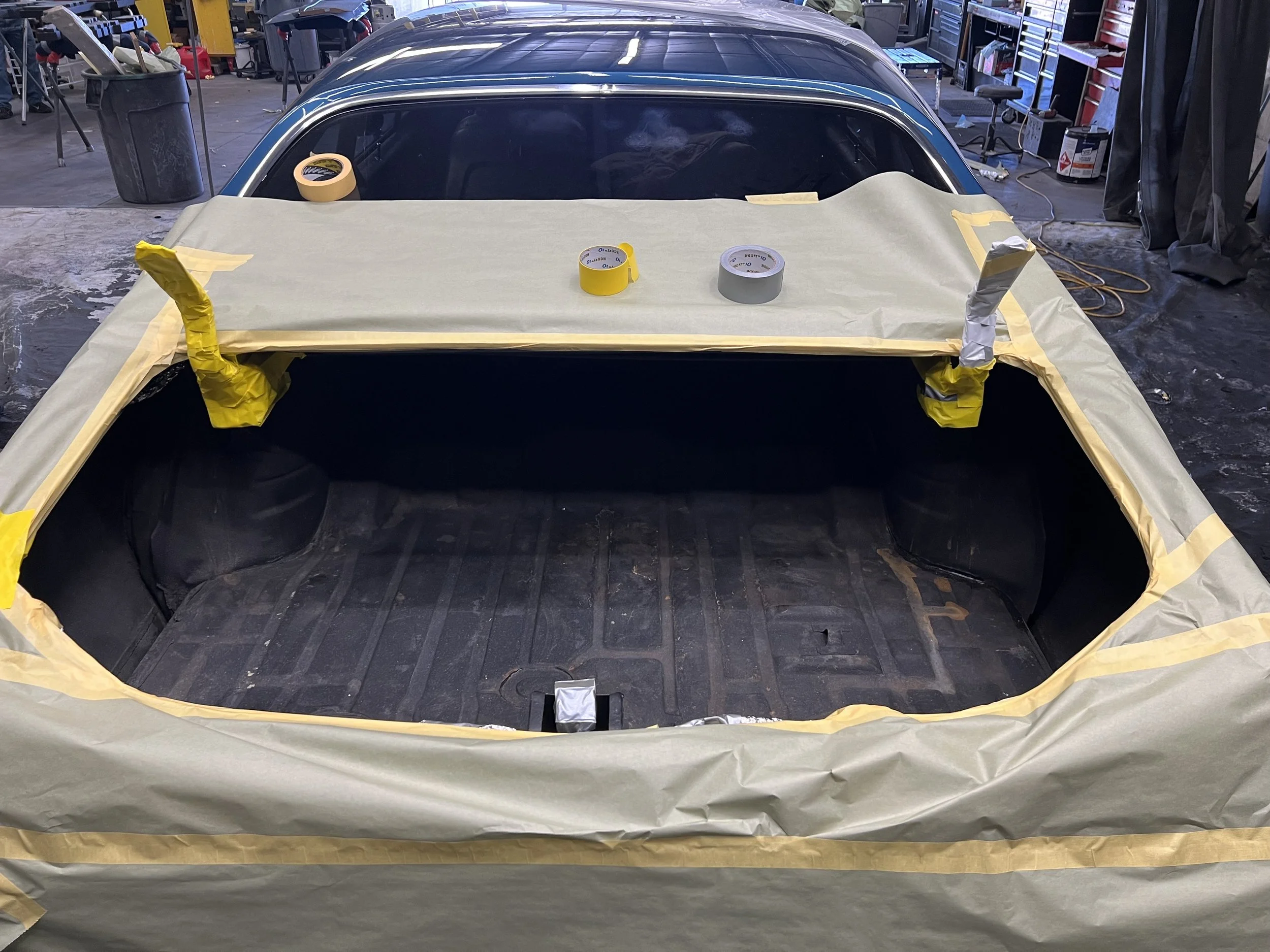 Car trunk area masked with painter's tape and paper, ready for painting or repair, in an auto workshop.