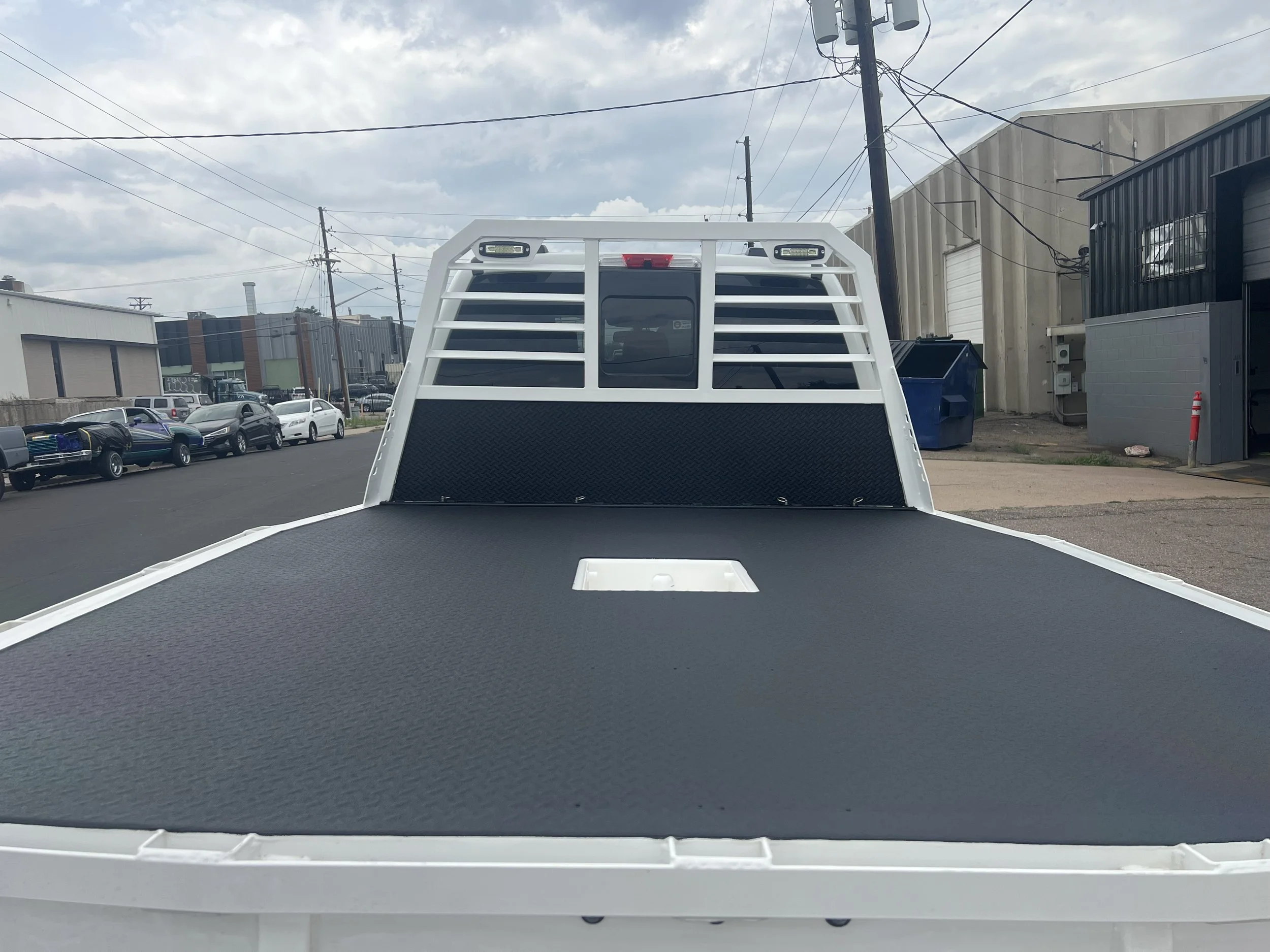 Empty flatbed truck with a Mil+Spec bed liner, view from rear, parking lot background.