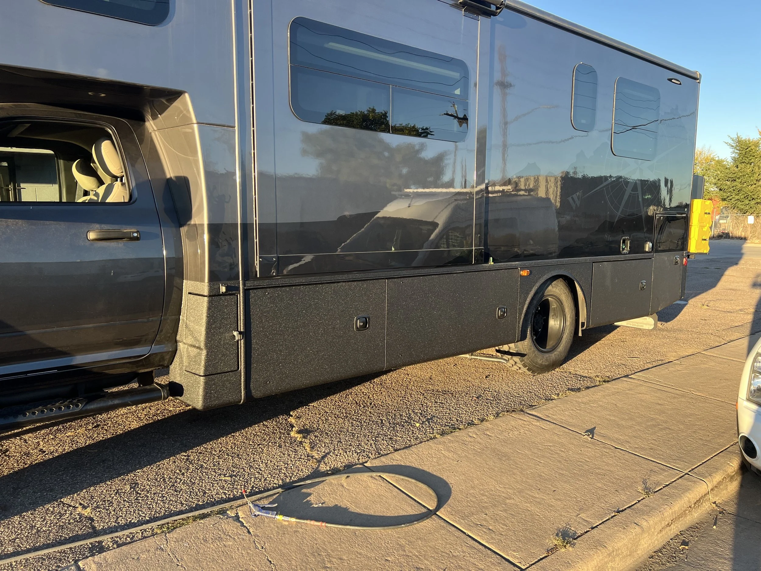 A black electric delivery vehicle parked on a city street during daylight, with reflections on its surface and a panoramic window on the side.