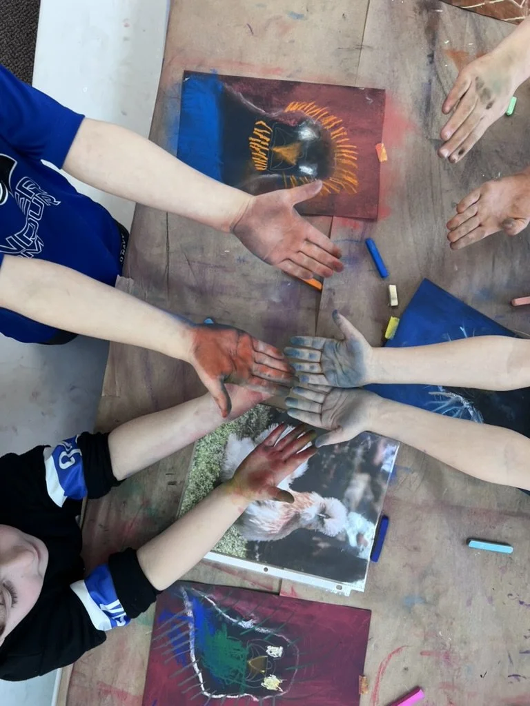 Children with painted hands gathered around a table, displaying art projects including images of a lion, a duck, and a spider.