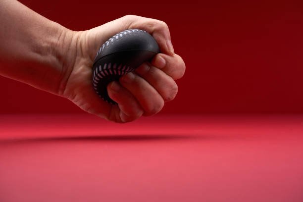 Close-up of a hand holding a black object with a patterned design, against a red background.