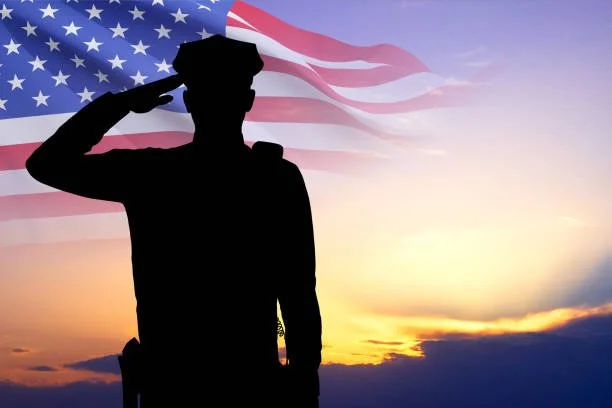 Silhouette of a soldier saluting in front of an American flag during sunset.