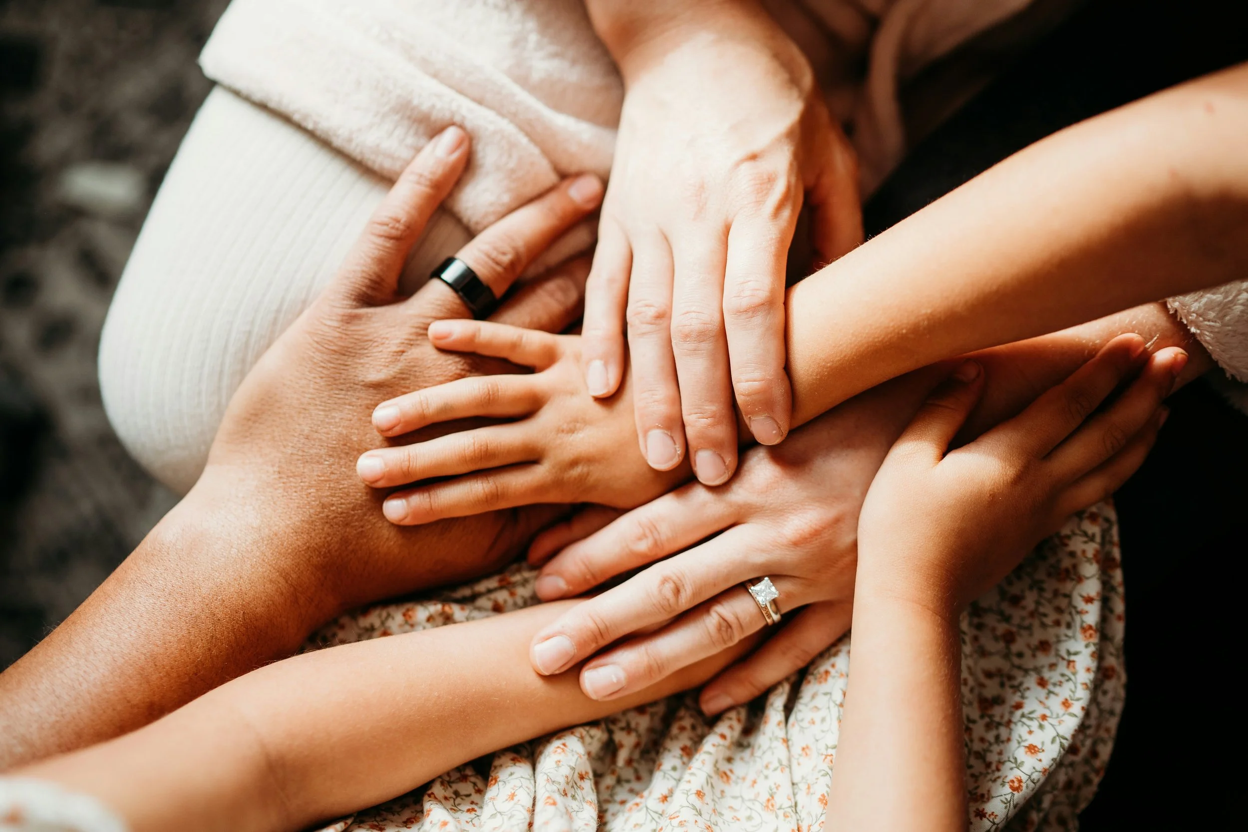 Multiple hands of diverse skin tones, some with rings, placed on top of each other in a gesture of unity and support.