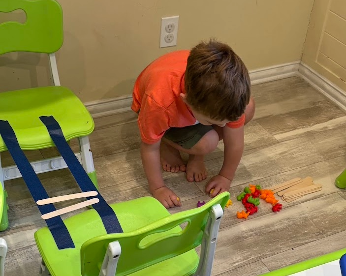 Child kneeling on the floor playing with small colorful toys next to green chairs and a beige wall.