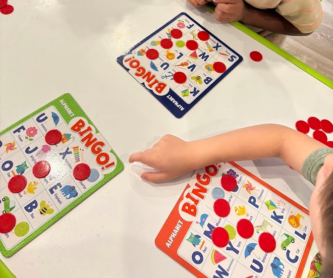 Children playing bingo with colorful alphabet-themed bingo cards on a white table.